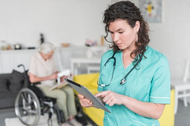 Free photo female nurse using digital tablet standing in front of senior woman sitting on wheelchair